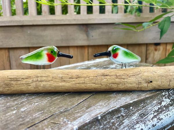 Charger l'image dans la galerie, Two small pocket sized green, red and white glass hummingbird figurines on a driftwood perch with a natural background