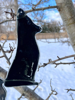A black glass dog ornament hangs from a tree. It's a snowy scene.