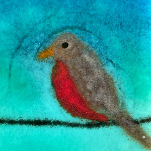 Close up of a red robin with a gold beak. The bird is made of glass and is a picture on a coaster.