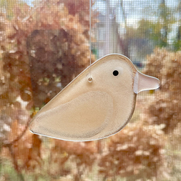 Load image into Gallery viewer, A champagne peachy pink glass bird hanging in a window. In the background are some dried hydrangea blossoms.