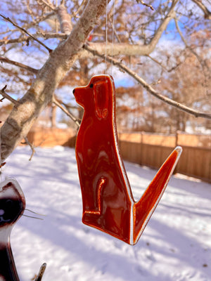 A chestnut conker brown glass dog hangs from a tree. It's a snowy scene.