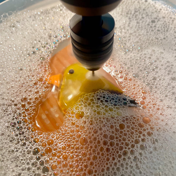 Load image into Gallery viewer, Close up of a fused glass bird ornament being drilled in a water bath