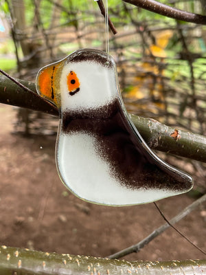 Decorative glass black and white puffin hanging bird ornament on a branch