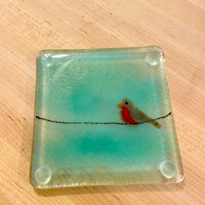 Square fused glass coaster with a bird design on a wooden surface