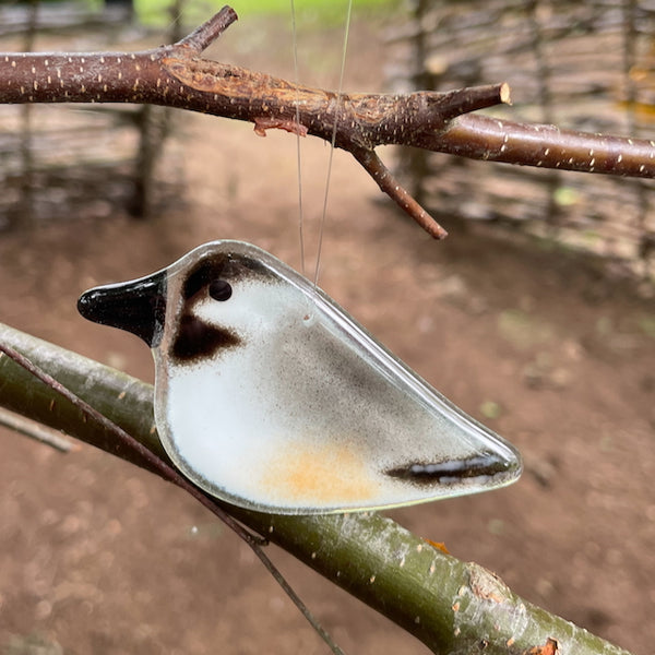 Load image into Gallery viewer, A grey, white and black chick sized fusedg glass chickadee hanging ornament, hanging in the garden