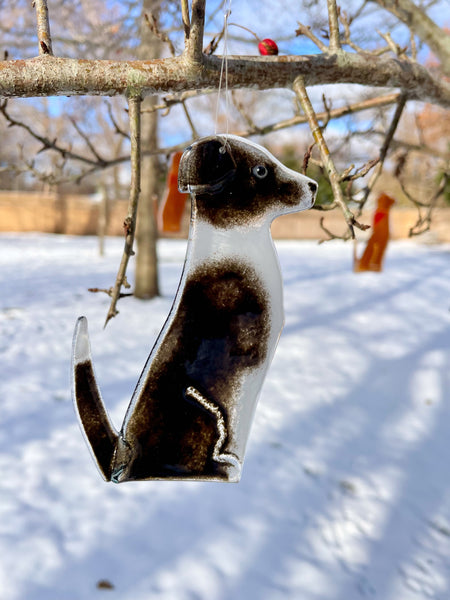 Load image into Gallery viewer, A black and white glass dog in the form of a border collie bandana hangs from a tree. It's a snowy scene. This dog is Dog B of a series of Dog designs.
