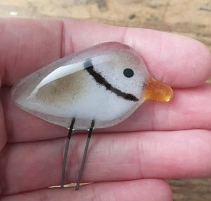 A tiny brown and white glossy glass piping plover fits in the palm of a hand