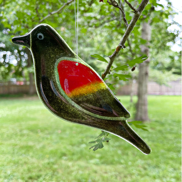 Load image into Gallery viewer, Decorative red winged blackbird glass bird with a red wing hanging from a tree branch outdoors.