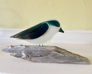 A close up of a deep aqua blue glass tree swallow on a driftwood perch.