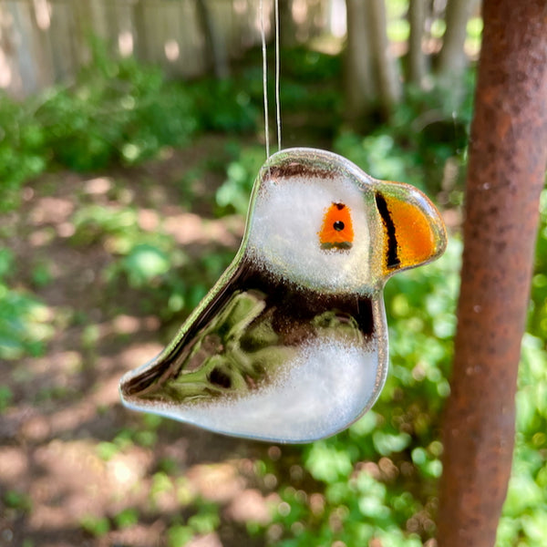 Load image into Gallery viewer, black and white fused glass hanging puffin chick against a background of woodland nature