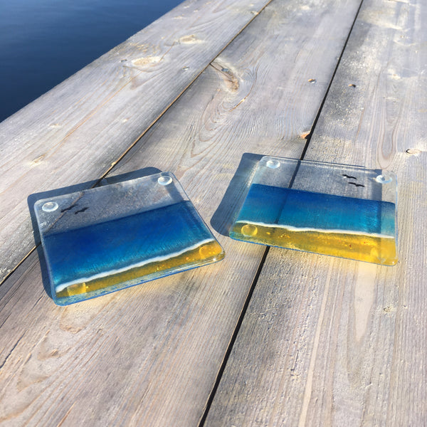 Load image into Gallery viewer, a pair of beach themed coasters made from fused glass