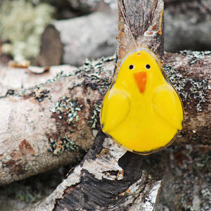 a fused glass yellow chick with wings hangs in front of an old log