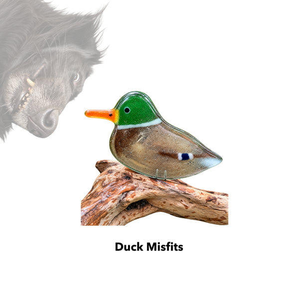Load image into Gallery viewer, a fused glass mallard on a driftwood perch. the ornament is shown simply on a white background. There an opaque picture of goofy black shepherd dog in the background.