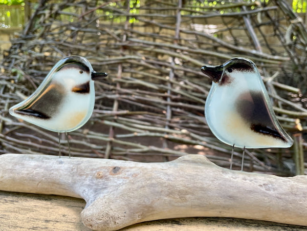 Charger l'image dans la galerie, Pair of Black, White and Peach Adult Size Chickadee Fused Glass Birds, perched on driftwood, against a backdrop of garden branches