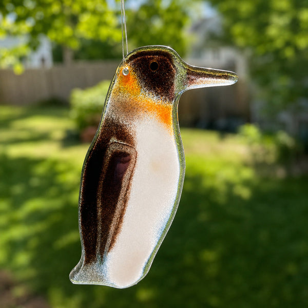 Charger l'image dans la galerie, A black, orange and white glass hanging penguin is suspended in a sunny window