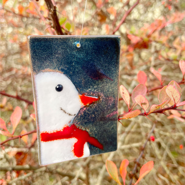 Load image into Gallery viewer, Decorative glass blue ornament featuring a snowman design hanging among autumn-winter leaves.
