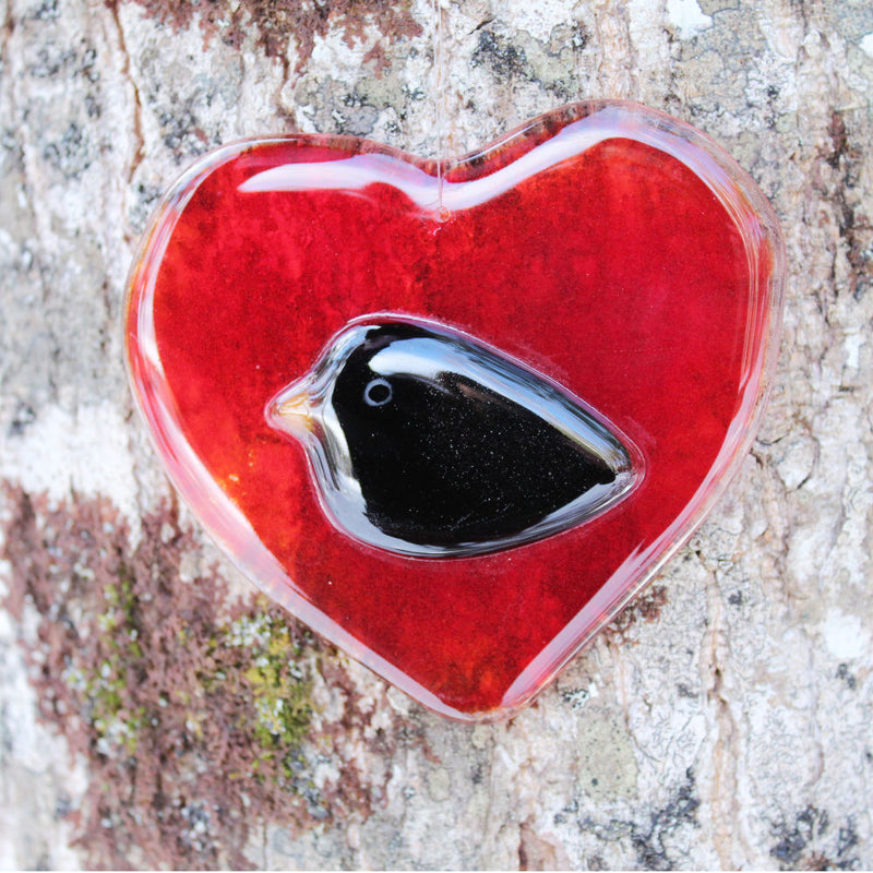 red fused glass heart with a blackbird in the centre.