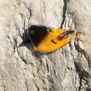 An orange and black Fused Glass Baltimore Oriole Hanging Ornament hangs in front of a rock