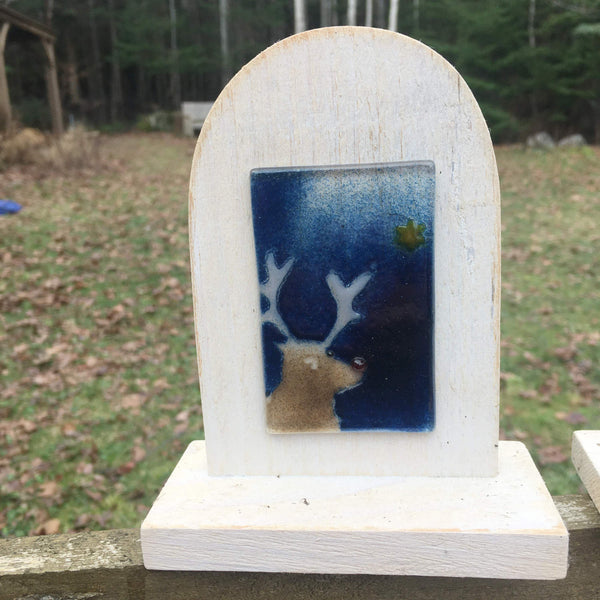 Load image into Gallery viewer, An ivory coloured wooden arch-shaped stand with a fused glass tile on the front. The tile features a reindeer looking at a star in a midnight blue sky.