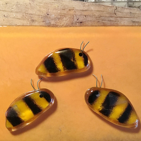 Load image into Gallery viewer, Three Gold and Black Glass Honey Bee with an iridescent wing sit on a peach coloured piece of glass