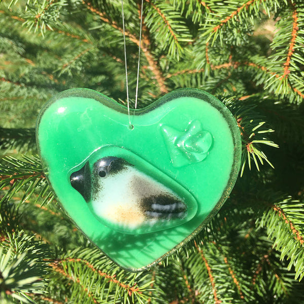 Load image into Gallery viewer, A Green Fused Glass Heart with Chickadee hangs in front of a Christmas Tree