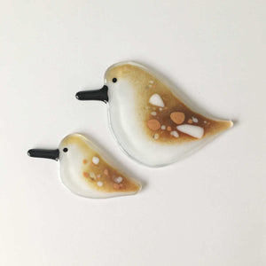 Two fused glass hanging sandpipers, one adult and one chick, lay side by side. They're brown and white mottled patterned.