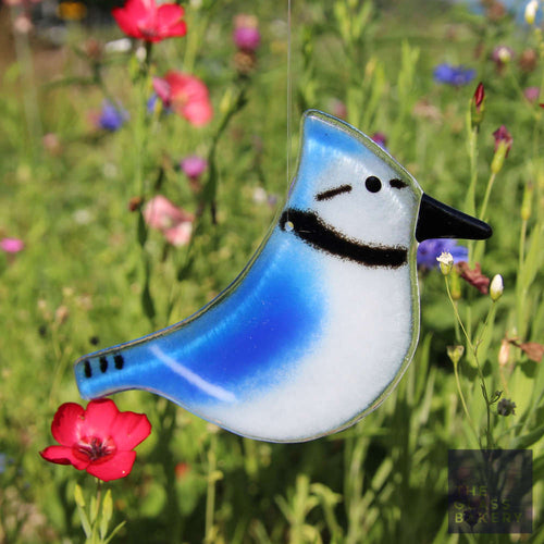 A glass bluejay ornament hangs in front of red and purple wildflowers