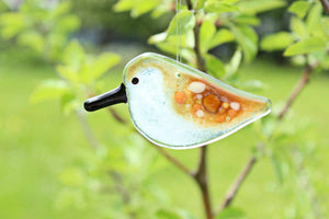 A brown and white speckled fused glass sandpiper chick hangs on a branch