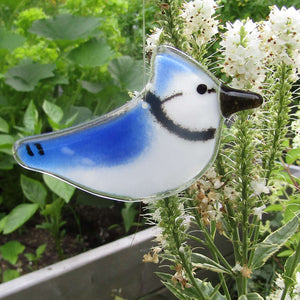 Small blue and white glass blue jay bird hangs in front of some white flowers