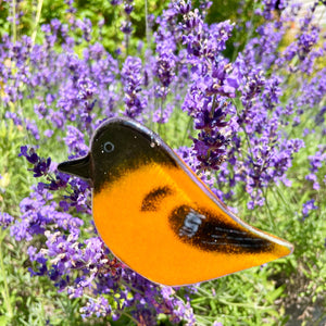 Decorative orange and black bird-shaped glass ornament in front of lavender flowers