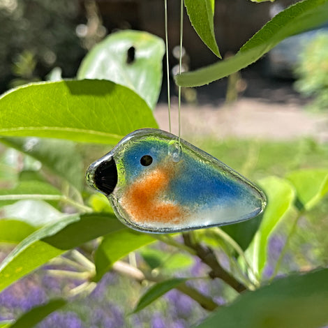 orange and blue used glass pocket sizedbluebird hanging in a tree