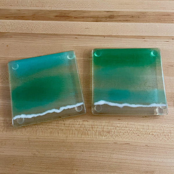Load image into Gallery viewer, Two square teal coasters with a white foamy sea accent on a wooden surface
