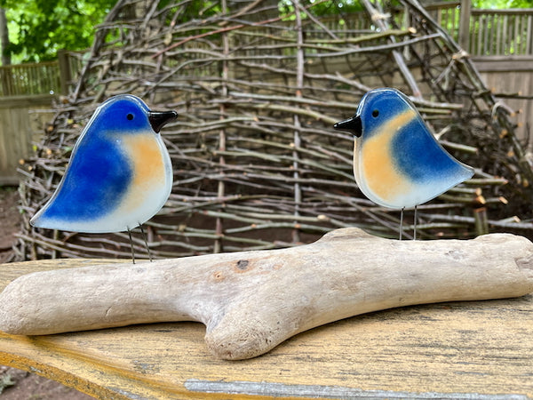 Load image into Gallery viewer, A pair of blue, white and peach fused glass bluebirds on driftwood, in nature
