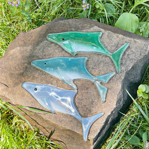 Three fused glass whales are placed on a garden rock