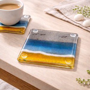 Glass coaster with gradient beach themed design on a wooden surface