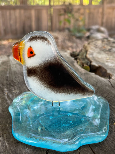 Black and White fused glass bird figurine on a glass iceberg, placed on a tree stump with a blurred natural background