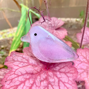 A blossom pink glass bird hanging in front of pinky-red Astibe