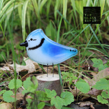 Load image into Gallery viewer, A small blue and white glass blue jay bird sits on a log in amongst green foliage.
