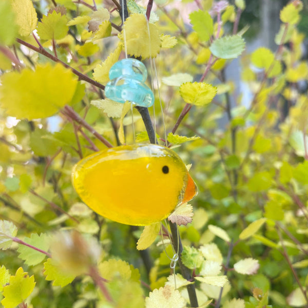 Load image into Gallery viewer, Yellow bird-shaped ornament hanging from a branch with green leaves
