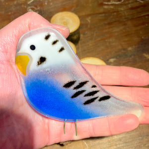 a glass blue budgie sits on the palm of an artisan