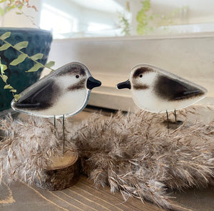 Two decorative chickadee bird figures on stands in a cozy feel habitat on a shelf