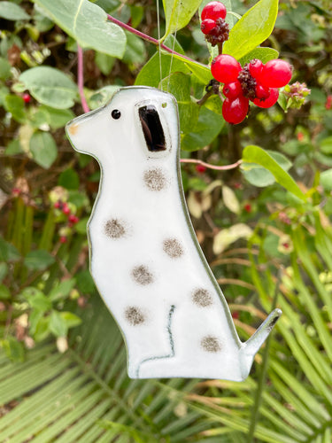 A black and white spotted fused glass do ornament is hanging in front of some honeysuckle