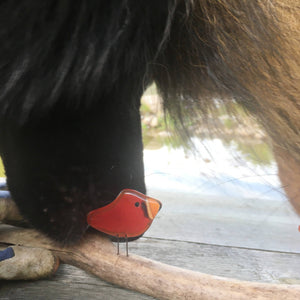 a black dog is trying to pick up a stick which has a glass red bird on it