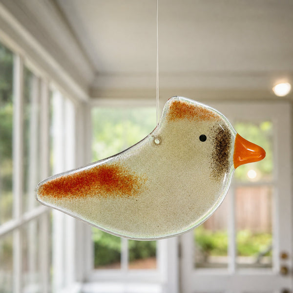 Charger l'image dans la galerie, A hanging female cardinal bird-shaped glass ornament with a speckled cream body, rust-orange wing and head markings, and an orange beak, suspended indoors in front of softly blurred windows.
