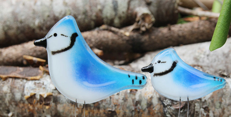 Two blue and white handcrafted glass bluejays sit in front of some foliage