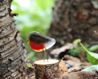 A red and brown studio glass robin bird sits on a log with woodland as a backdrop