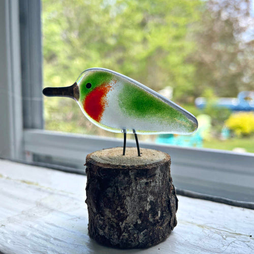 A ruby throated hummingbird made from glass sits on a window ledge