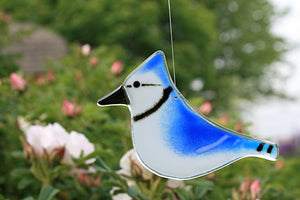 a blue and white fused glass bluejay bird hangs in front of pink roses