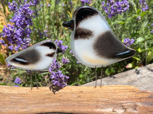 Two black and white glass bird figurines on a wooden log with purple flowers in the background