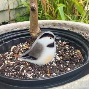 A black, grey and white fused glass adult chickadee is perched in a planter